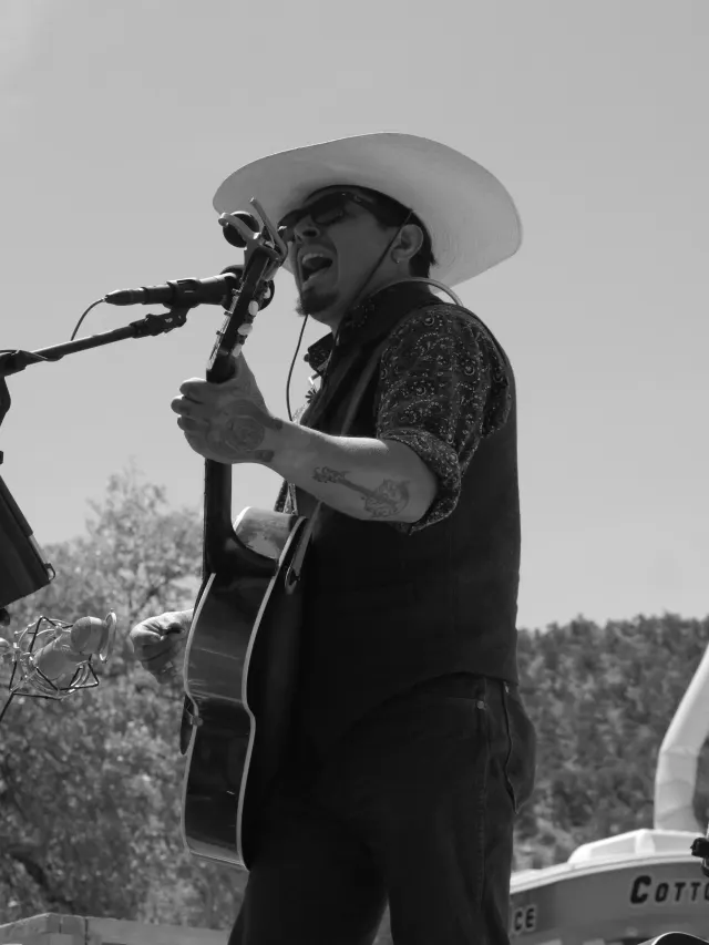 Black and white photo of Rooster singing into a microphone with a guitar.