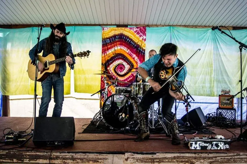 Two musicians on an outdoor festival stage under a painted backdrop.