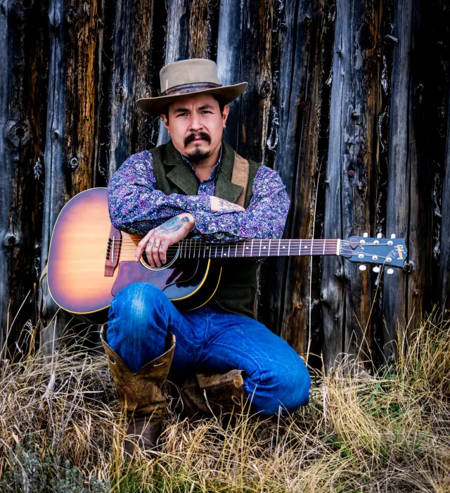 Rooster crouched in tall grass holding an acoustic guitar.